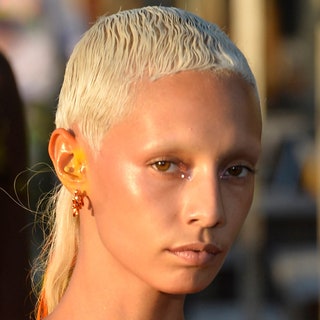 Woman with golden makeup on her ears and inner corner of eyes and blonde buzz cut 